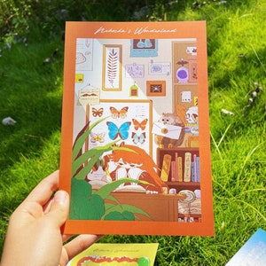 May include: An orange postcard with an illustration of a study scene. It depicts a butterfly chart, an owl with a letter, and a person reading. The text "Rebekah's Wonderland" is at the top of the postcard.
