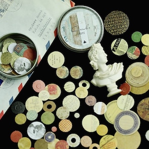 May include: A collection of circular paper ephemera in various colors and patterns, including stamps, maps, and text. A white bust and a tin with the text "Circuler 100 pic" are also present. An envelope with text is in the background.