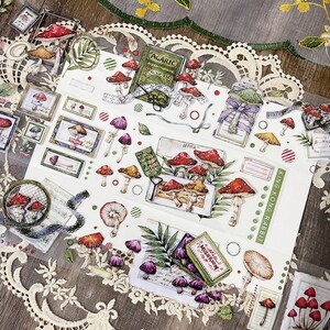 May include: A sheet of decorative stickers featuring illustrations of mushrooms, leaves, and other forest elements. The stickers are printed on a white background with a variety of colors, including red, green, brown, and purple. The stickers are perfect for adding a touch of whimsy to journals, planners, and other craft projects.