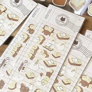 May include: Clear plastic sheets filled with various bread-themed stickers. The stickers feature cartoon bread slices, some with faces, and other food-related illustrations. The text "MEWMEWBEAM VINTAGE STICKER" is printed on the sheets.