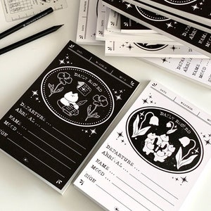 May include: Two black and white daily record notebooks with a whimsical design featuring a cat and flowers. The notebooks have a black background with white text and illustrations. The text on the notebooks reads "Daily Record".