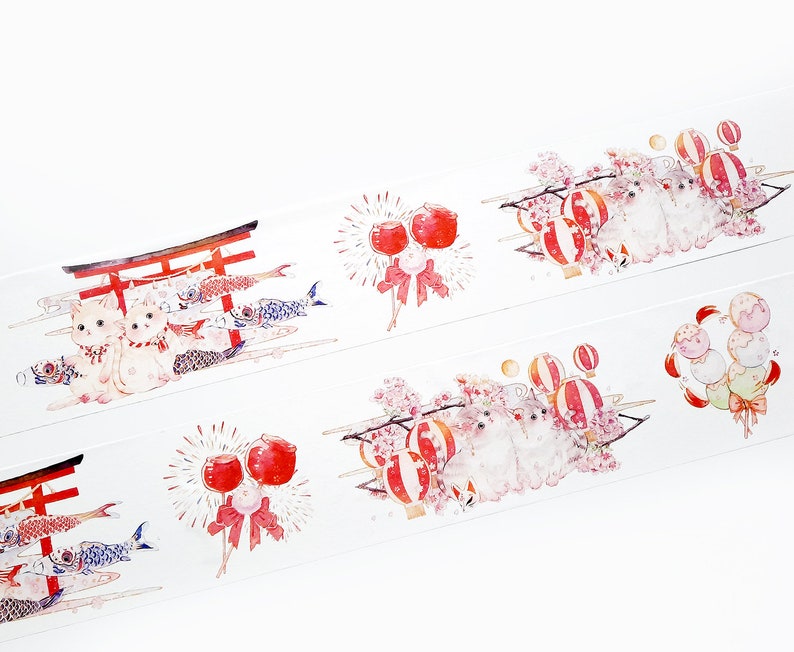Puede incluir: Cinta washi blanca con un patr&oacute;n repetido de linternas rojas y blancas, flores de cerezo, gatos y manzanas de caramelo rojas y blancas. La cinta tambi&eacute;n presenta una puerta torii roja con dos gatos blancos y peces koi nadando en el agua.