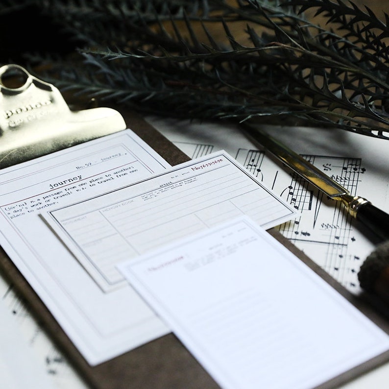 May include: A close-up of a clipboard with two blank white paper forms. The forms have lines and headings, including "Journey" and "No. 57". The clipboard is on a brown surface with a sheet of music and a silver letter opener.