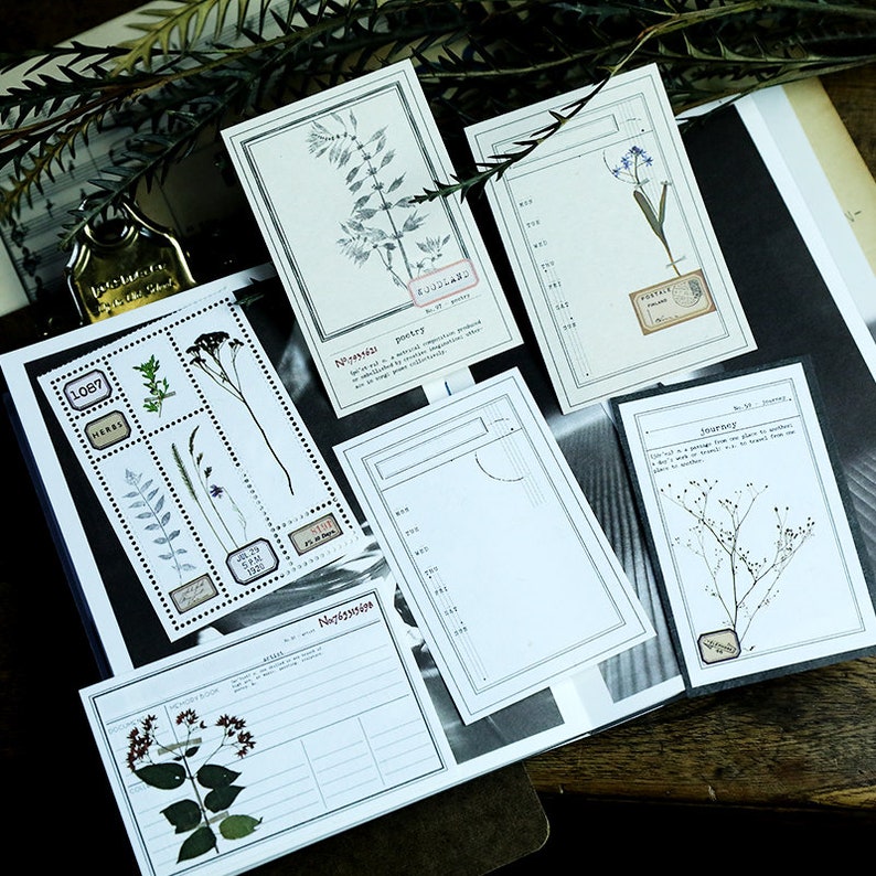 May include: Set of six blank cards with botanical illustrations and text. The cards feature pressed flowers and leaves, with titles like "Nostalgia", "Poetry", "Journey", and "Herbs".