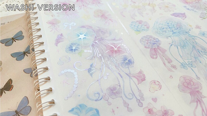 Puede incluir: Una hoja de cinta washi transparente con un acabado hologr&aacute;fico que presenta un patr&oacute;n repetitivo de medusas azul pastel y rosa, flores y remolinos. El texto "WASHI VERSION" est&aacute; impreso en la parte superior de la hoja.