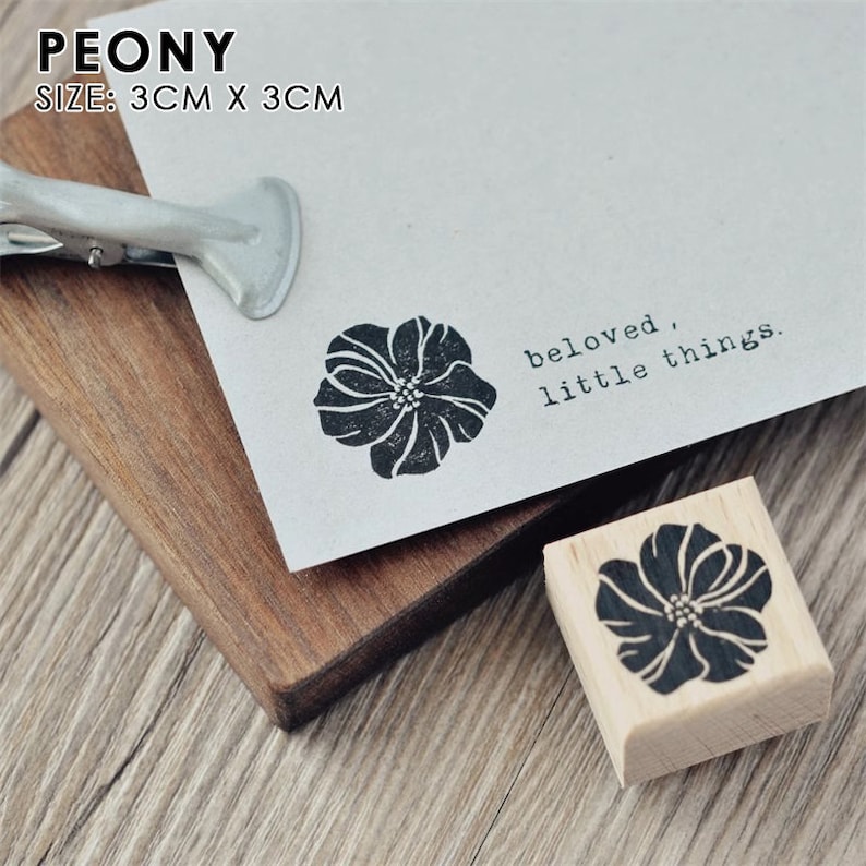 May include: A wooden stamp with a black and white image of a peony flower. The stamp is 3 cm x 3 cm and reads "beloved, little things".