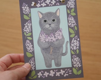 Puede incluir: Un gato gris sosteniendo un ramo de flores moradas, rodeado de un borde de hojas verdes y flores moradas sobre un fondo azul claro.