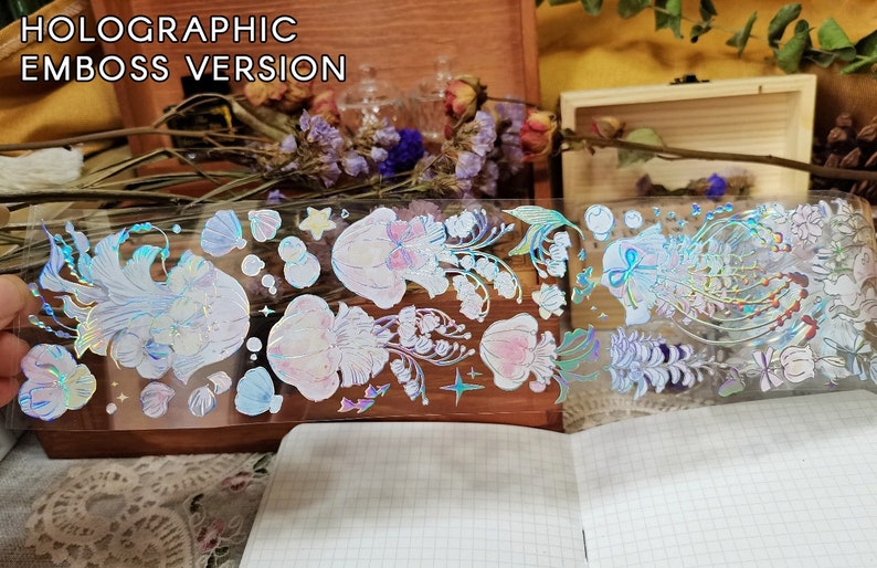 Puede incluir: Una hoja de pegatinas hologr&aacute;ficas con acabado en relieve. Las pegatinas presentan una variedad de dise&ntilde;os, incluyendo flores, conchas y estrellas. Las pegatinas son iridiscentes y tienen un efecto arco&iacute;ris.