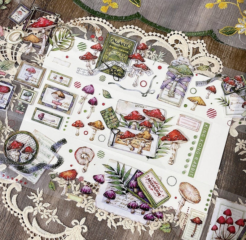 May include: A sheet of decorative stickers featuring illustrations of mushrooms, leaves, and other forest elements. The stickers are printed on a white background with a variety of colors, including red, green, brown, and purple. The stickers are perfect for adding a touch of whimsy to journals, planners, and other craft projects.