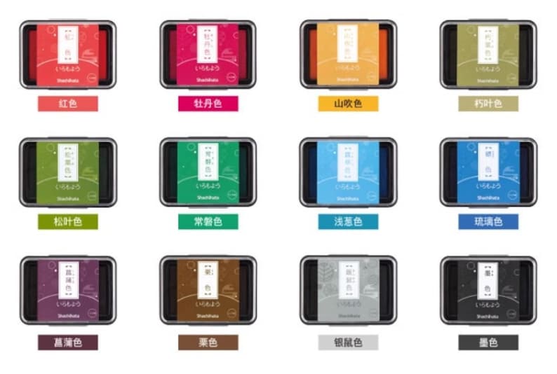 May include: A collection of twelve ink pads in various colors, each in a rectangular black case. The pads feature Japanese text and color names, including red, pink, orange, green, blue, and purple.