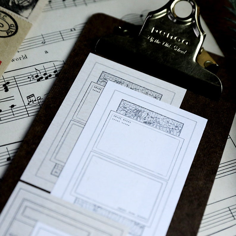 May include: Three blank travel journal pages with a decorative border featuring a stylized map. The pages are on a clipboard with a vintage-style clip.