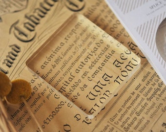 May include: Close-up of a vintage document with the text "Land Tobacco" and "Capital Autorizado 2.000.000" in black ink. The document is on a brown surface with a clear glass paperweight on top.