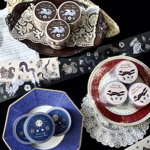May include: Several rolls of decorative adhesive tape featuring intricate illustrations of winged rabbits, foxes, and celestial motifs. The labels on the rolls display the text "Order of the Whispering Rune" alongside various animal and star graphics.