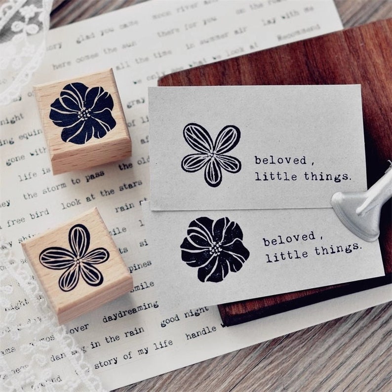 May include: Four wooden stamps with floral designs and the text "beloved, little things." The stamps are on a light brown surface.