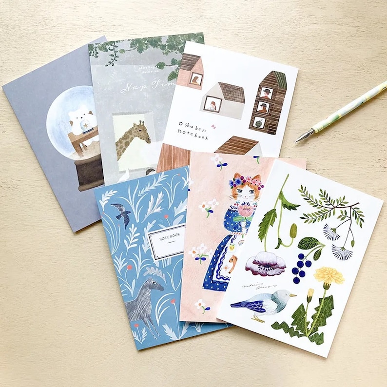 Puede incluir: Una colecci&oacute;n de seis peque&ntilde;os cuadernos ilustrados con varios dise&ntilde;os. Los cuadernos presentan un gato, una jirafa, un p&aacute;jaro, una casa, una bola de nieve y un patr&oacute;n floral. El texto en los cuadernos dice "Oh so best notebook".