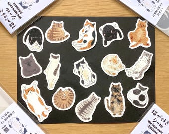 May include: A selection of cat stickers in diverse poses and colours, including black, orange, and tabby patterns. The stickers are displayed on a black surface, with packaging that reads "We love cats Stickers" in English and Japanese.