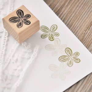 May include: A wooden stamp with a black floral design. The stamp is used to create impressions of the flower design in different shades of green.
