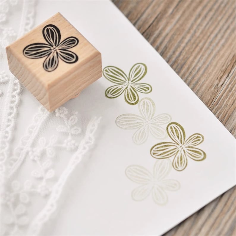 May include: A wooden stamp with a black floral design. The stamp is used to create impressions of the flower design in different shades of green.