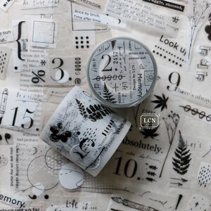 May include: A roll of decorative washi tape with a black and white fern pattern. The tape is on a white background with other washi tape rolls and paper scraps. The text on the tape reads "Memory" and "Life is..."