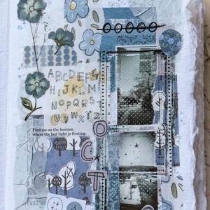 May include: A mixed media art journal page with a collage of blue and white patterned papers, floral elements, and handwritten text. The page includes the letters of the alphabet, the word "OCT", and the numbers "09". The text "Find me on the horizon where the last light is fleeting" is also present.