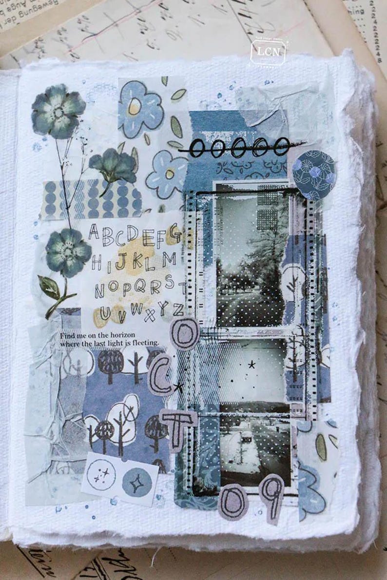 May include: A mixed media art journal page with a collage of blue and white patterned papers, floral elements, and handwritten text. The page includes the letters of the alphabet, the word "OCT", and the numbers "09". The text "Find me on the horizon where the last light is fleeting" is also present.