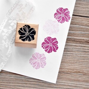 May include: A wooden stamp with a black floral design. The stamp is used to create pink floral impressions on paper.