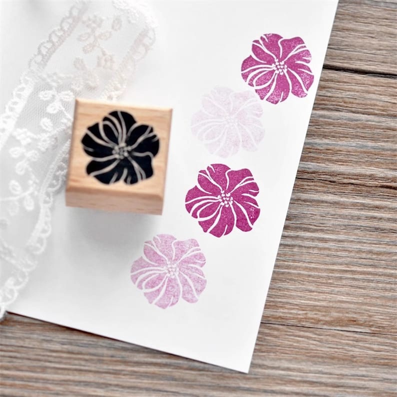 May include: A wooden stamp with a black floral design. The stamp is used to create pink floral impressions on paper.