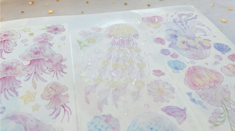 Puede incluir: Una hoja de pegatinas transparentes con un dise&ntilde;o de acuarela de medusas, flores y otras criaturas marinas. Las pegatinas son perfectas para a&ntilde;adir un toque de fantas&iacute;a a tu agenda, diario o &aacute;lbum de recortes.