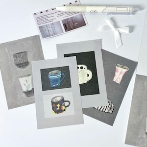 Puede incluir: Una variedad de impresiones artísticas ilustradas con tazas y jarrones en varios diseños y colores. También hay un bolígrafo blanco y una tarjeta pequeña con texto e imágenes, junto con una cinta blanca.