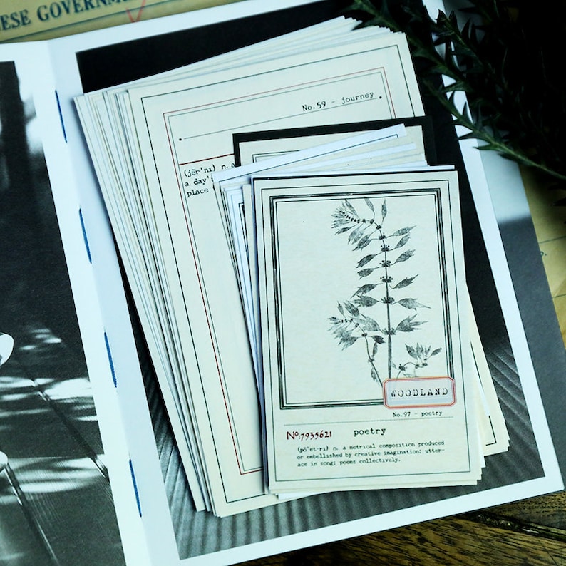 May include: A stack of vintage-style cards with black borders and handwritten text. The top card features a black and white illustration of a plant with the text "WOODLAND No. 97 poetry" and "N&deg; 7939621 poetry (def'n) a metrical composition, produced or embellished by creative imagination: utterance in song; poems collectively".