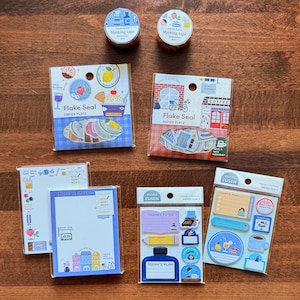 May include: Two rolls of masking tape, two packs of Flake Seal stickers, two memo pads, and two packs of mini fusen sticky notes. The stationery items feature colorful illustrations of food, drinks, buildings, and text like Flake Seal and Papier Platz.