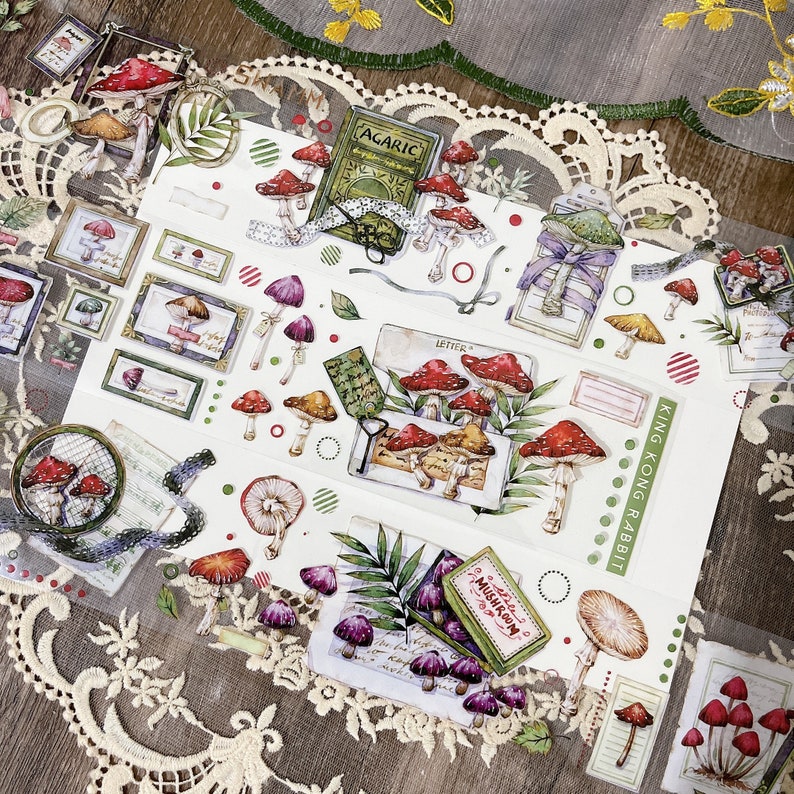 May include: A sheet of colorful stickers featuring illustrations of mushrooms, leaves, and other nature-inspired designs. The stickers are perfect for adding a touch of whimsy to journals, planners, and other craft projects. The stickers include the text "King Kong Rabbit" and "Mushroom".