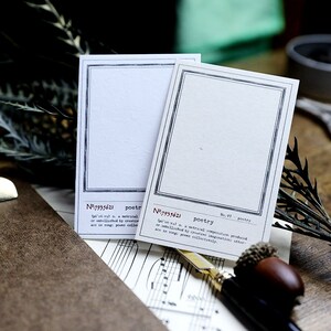 May include: Two blank white cards with black borders and a decorative design. The cards have the text "No:7935621 poetry" and "No.97 poetry" printed on them. The cards are on a brown surface with musical notes printed on it.