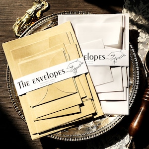 Puede incluir: Una pila de sobres marrones con una etiqueta blanca que dice "THE ENVELOPES" y una pila de sobres blancos con una etiqueta blanca que dice "ELOPES".