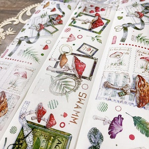 May include: A set of four washi tapes featuring a mushroom and forest theme. The tapes have a white background with illustrations of mushrooms, leaves, and other forest elements. The text "SWAMM" is printed on one of the tapes.