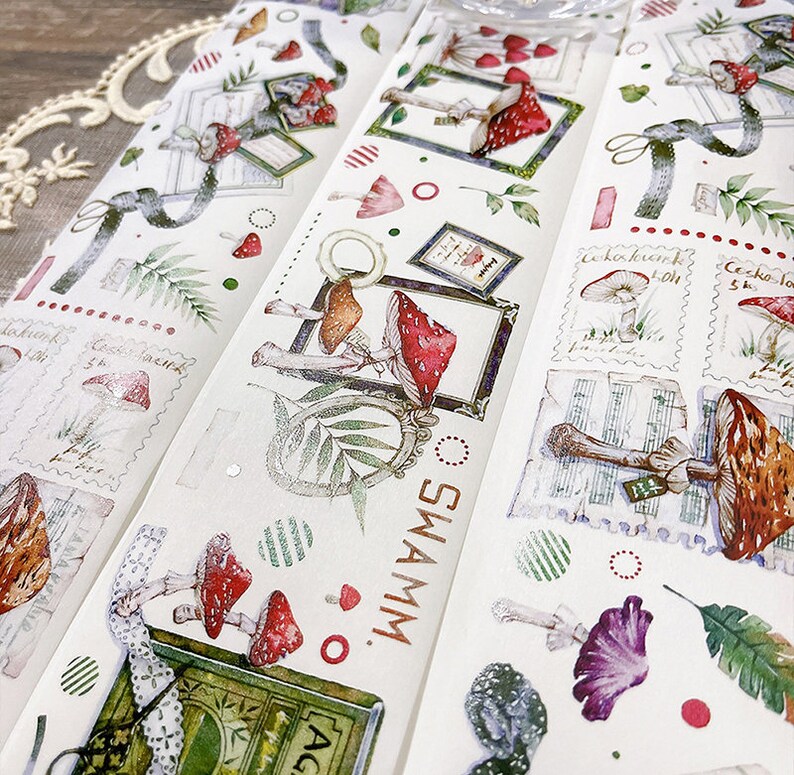 May include: A set of four washi tapes featuring a mushroom and forest theme. The tapes have a white background with illustrations of mushrooms, leaves, and other forest elements. The text "SWAMM" is printed on one of the tapes.