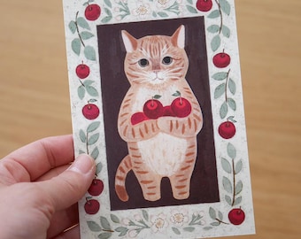 Könnte beinhalten: Eine braune und weiße Tabby-Katze mit orangefarbenen Streifen hält drei rote Äpfel in ihren Pfoten. Die Katze steht in einem braunen Rahmen mit einem grünen Blatt-Rand und roten Äpfeln um den Rahmen herum. Der Hintergrund ist weiß mit kleinen weißen Blüten.