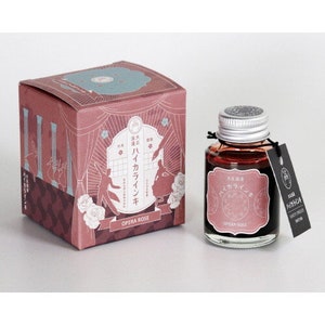 May include: A bottle of Opera Rose ink, a dark red ink with a pink and white label. The label features Japanese text and the words "Opera Rose". The bottle is sitting on a white surface.