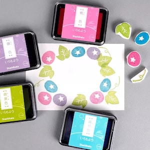 May include: A collection of Shachihata ink pads in various colors, including pink, purple, green, and blue, with matching stamps. The stamps create a floral design with star-shaped centers and leaf accents. The text "いろもよう" is visible on the ink pads.