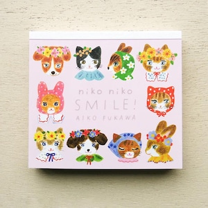 May include: A pink notepad featuring illustrated animal faces with floral crowns and bonnets. The notepad has the words "niko niko SMILE!" and "AIKO FUKAWA" printed on the front.