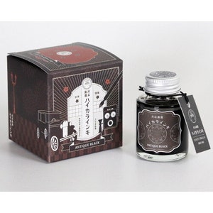 May include: A bottle of black ink with a silver lid and a label that says "Antique Black" and "Iro-Ai-zome" in Japanese. The bottle is sitting on a white surface.