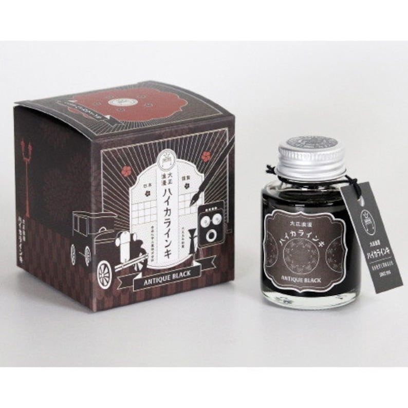 May include: A bottle of black ink with a silver lid and a label that says "Antique Black" and "Iro-Ai-zome" in Japanese. The bottle is sitting on a white surface.