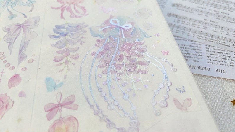 Puede incluir: Una hoja de pegatinas decorativas con una variedad de dise&ntilde;os florales en colores pastel, incluyendo glicinias, mariposas y lazos. Las pegatinas tienen un acabado hologr&aacute;fico, lo que les da un efecto brillante.
