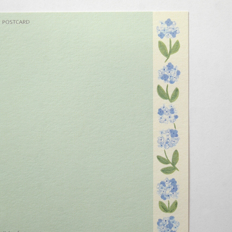 May include: A light green postcard with the word "POSTCARD" printed in the top left corner. The right edge of the postcard has a white border with a repeating pattern of blue flowers and green stems.