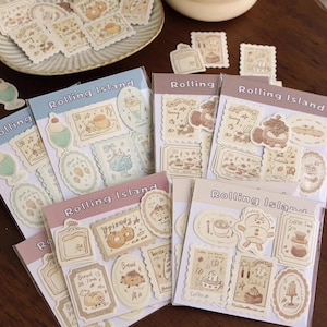 May include: Several sticker sheets with a vintage aesthetic, featuring illustrations of desserts, food, and characters. The stickers are in pastel colours, with some sheets displaying the text "Rolling Island".