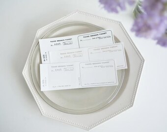 Puede incluir: Cuatro boletos blancos en blanco con el texto "Third Season Ticket" impreso en ellos. Los boletos están en un plato blanco con un borde de cuentas.
