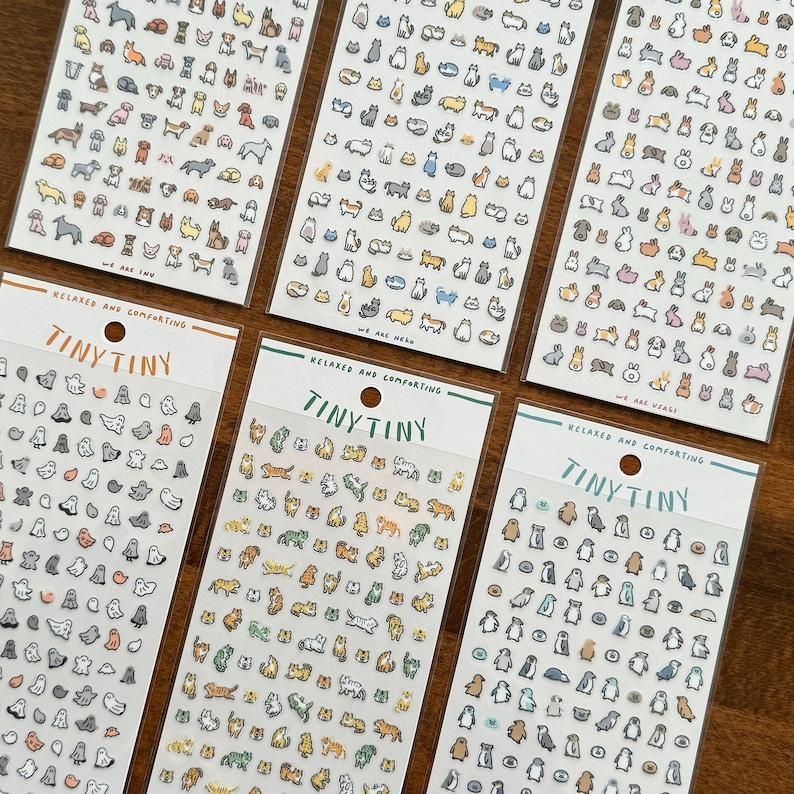 May include: Four sheets of stickers featuring various animal illustrations. Each sheet has a different theme: birds, cats, dogs, and penguins. The sheets are white with black text that reads "RELAXED AND COMFORTING" and "TINYTINY".