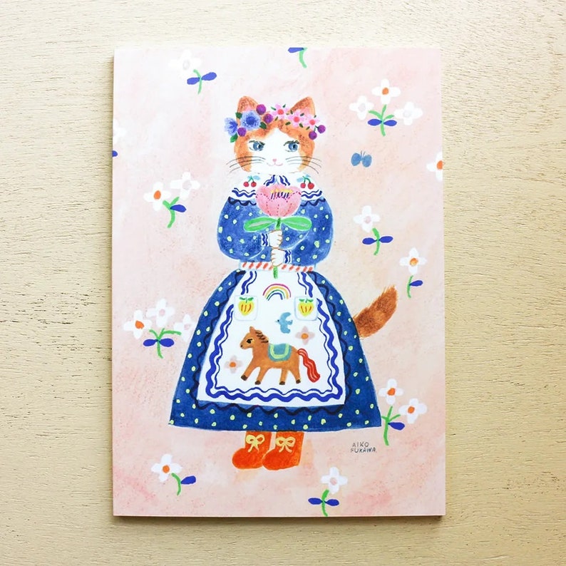 Puede incluir: Una ilustraci&oacute;n de dibujos animados de un gato con un vestido azul con estampado floral y una corona de flores. El gato sostiene una flor rosa y tiene un caballito de balanc&iacute;n en su delantal. El fondo es rosa con flores blancas.
