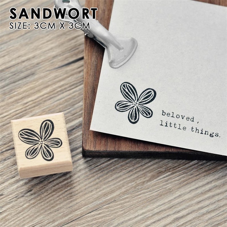 May include: A wooden stamp with a black and white flower design. The stamp is 3 cm by 3 cm and reads "beloved, little things".
