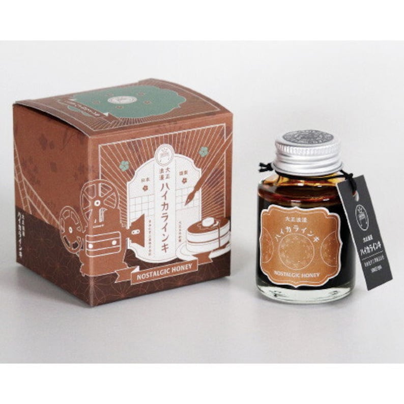 May include: A brown box with a film reel design and the text "Nostalgic Honey" on the front. A brown glass bottle of ink with a silver lid and the text "Nostalgic Honey" on the label.